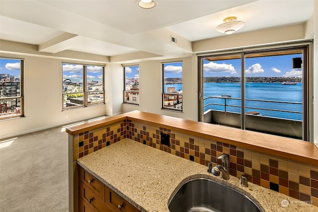 kitchen with sink, light stone counters, backsplash, a water view, and light carpet