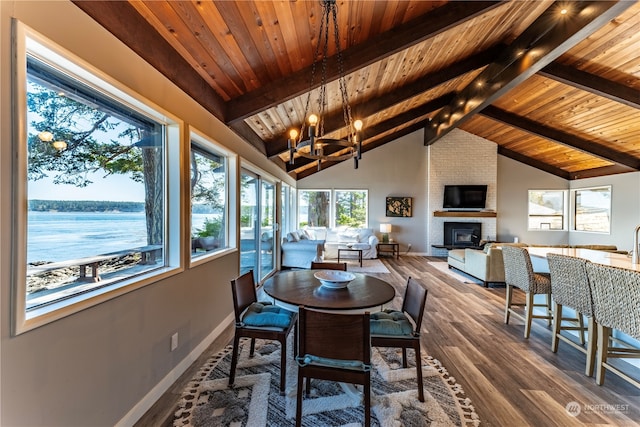 sunroom / solarium featuring wood ceiling, vaulted ceiling with beams, a water view, a notable chandelier, and a brick fireplace