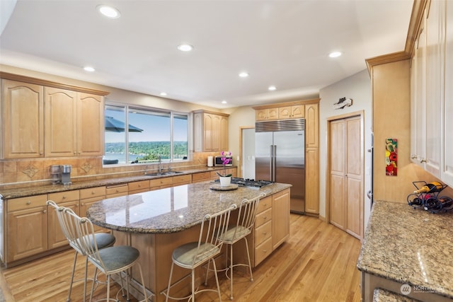 kitchen featuring appliances with stainless steel finishes, a breakfast bar, sink, light stone countertops, and light wood-type flooring