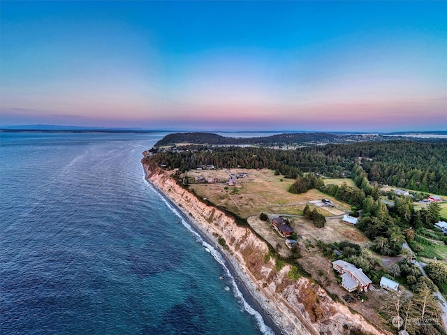 aerial view at dusk featuring a water view and a beach view