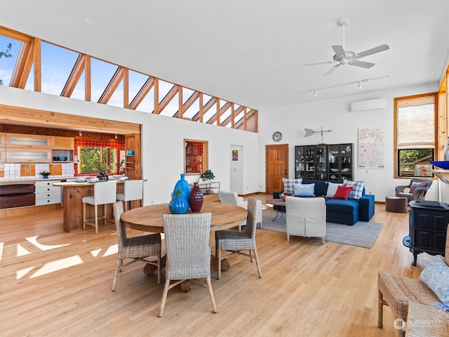 dining room featuring ceiling fan, a towering ceiling, rail lighting, a wall unit AC, and light hardwood / wood-style floors