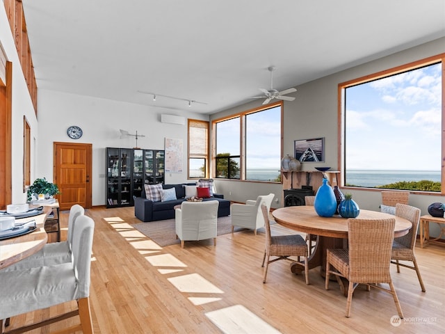 dining room featuring light wood-type flooring, track lighting, a water view, ceiling fan, and a wall unit AC