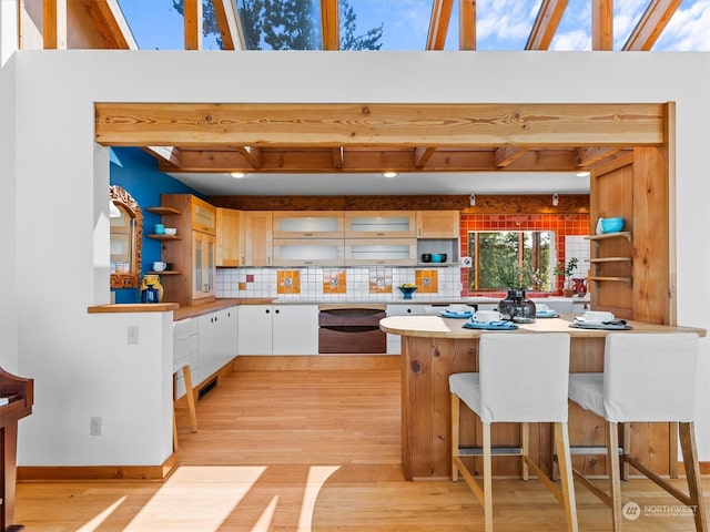 kitchen with a kitchen bar, light hardwood / wood-style flooring, white cabinetry, dishwashing machine, and tasteful backsplash