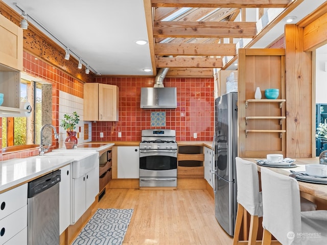 kitchen with light brown cabinets, stainless steel appliances, range hood, light hardwood / wood-style floors, and tasteful backsplash