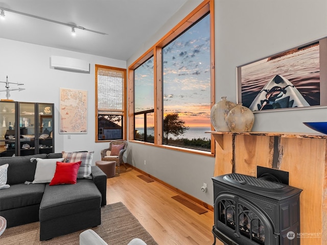 living room featuring light wood-type flooring, a wall mounted air conditioner, a wood stove, and rail lighting