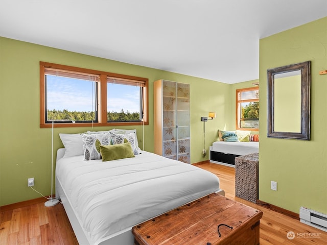 bedroom featuring baseboard heating, multiple windows, and light hardwood / wood-style floors