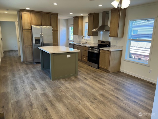 kitchen with wall chimney exhaust hood, sink, a center island, hardwood / wood-style flooring, and stainless steel appliances