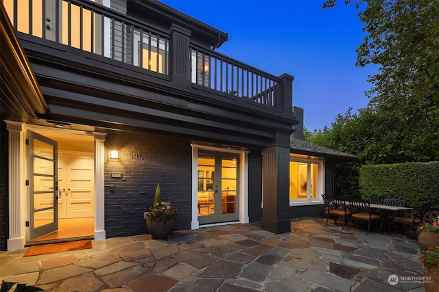 back house at dusk featuring a patio area, french doors, and a balcony