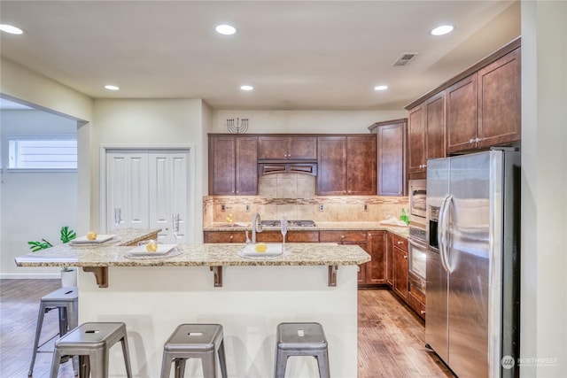 kitchen with a kitchen island with sink, stainless steel appliances, a kitchen bar, and light stone counters