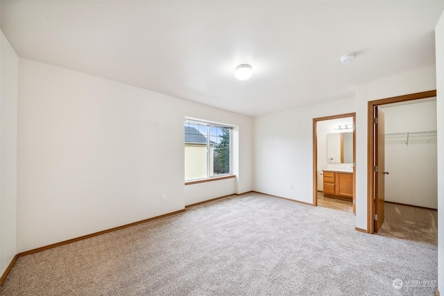 unfurnished bedroom featuring light colored carpet, a closet, ensuite bath, and a walk in closet