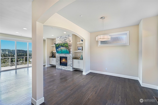 unfurnished living room featuring built in shelves, a stone fireplace, and dark hardwood / wood-style floors