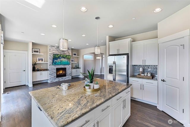 kitchen with stainless steel fridge with ice dispenser, tasteful backsplash, dark wood-type flooring, a kitchen island, and a stone fireplace