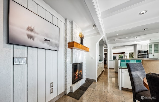 interior space featuring white cabinets, light tile patterned floors, a brick fireplace, appliances with stainless steel finishes, and beamed ceiling