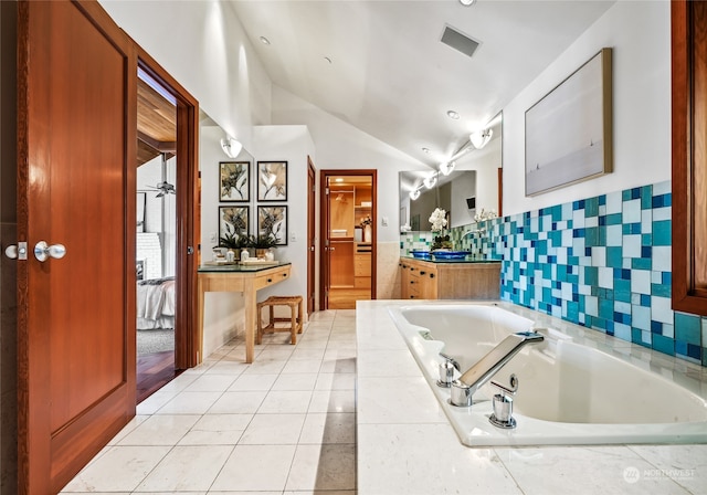 bathroom with tile patterned flooring, tiled bath, vaulted ceiling, and vanity