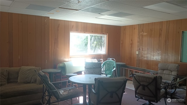 carpeted dining space featuring wood walls and a paneled ceiling