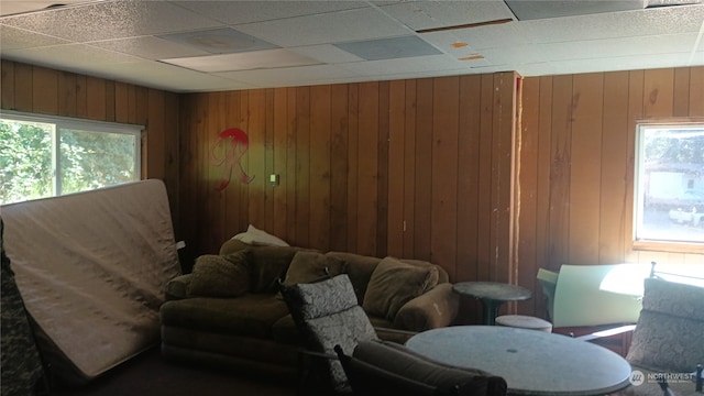 living room with a drop ceiling, wooden walls, and plenty of natural light