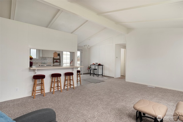 kitchen with lofted ceiling with beams, light carpet, a peninsula, decorative backsplash, and a kitchen bar