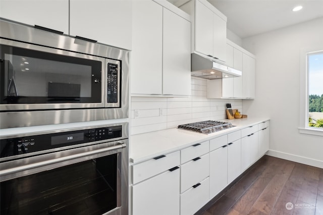 kitchen with white cabinetry, tasteful backsplash, dark hardwood / wood-style flooring, light stone countertops, and appliances with stainless steel finishes