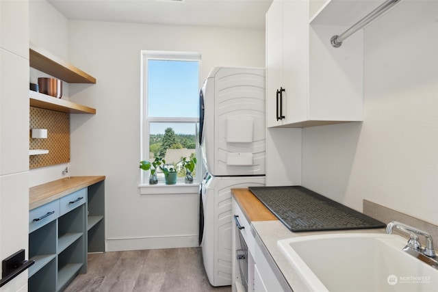 laundry area with sink, cabinets, stacked washer and clothes dryer, and light wood-type flooring