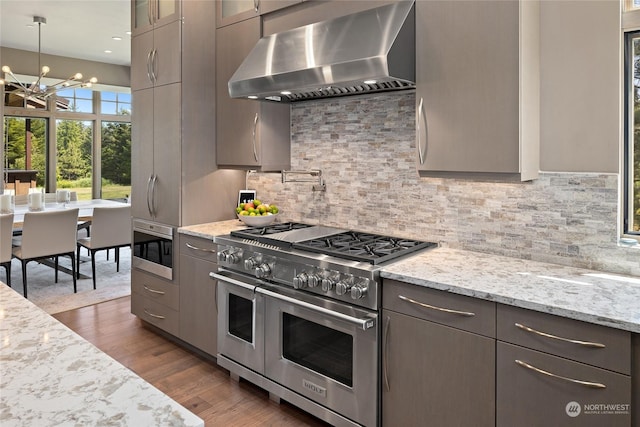 kitchen with light stone counters, hanging light fixtures, dark hardwood / wood-style floors, stainless steel appliances, and range hood