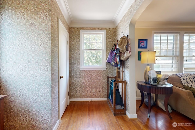 interior space with arched walkways, light wood-style flooring, baseboards, ornamental molding, and wallpapered walls