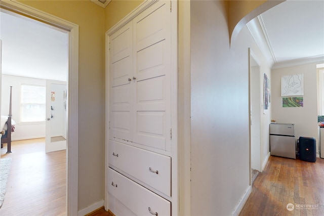 hallway featuring light wood-style floors, baseboards, arched walkways, and crown molding