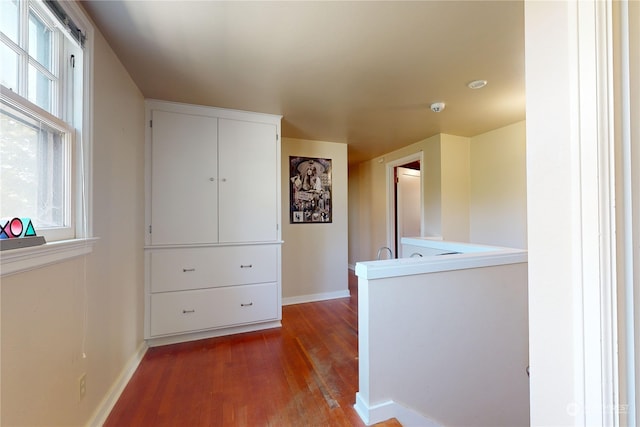 corridor with an upstairs landing, a healthy amount of sunlight, baseboards, and wood finished floors