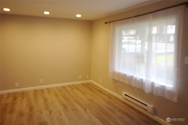 empty room featuring a baseboard heating unit and light hardwood / wood-style floors