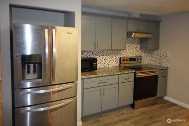 kitchen with hardwood / wood-style floors, wall chimney exhaust hood, appliances with stainless steel finishes, and backsplash