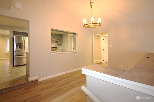 corridor with a notable chandelier, vaulted ceiling, and hardwood / wood-style floors