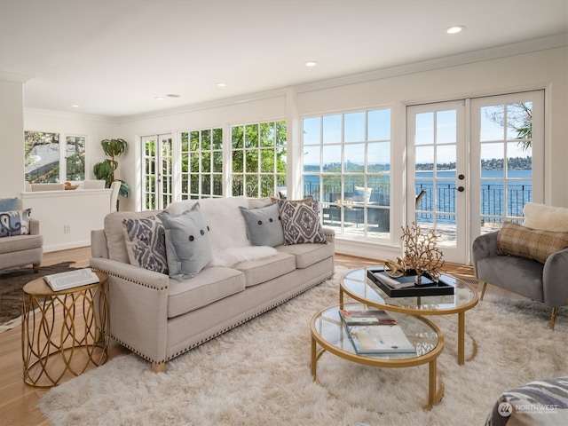 living room with a water view, light wood-type flooring, crown molding, and french doors