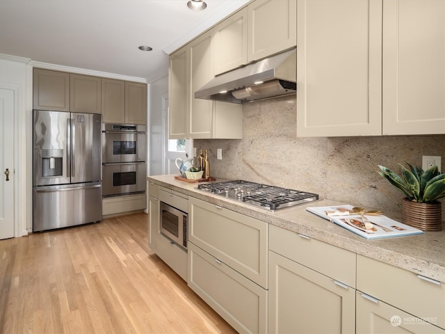 kitchen featuring light wood-type flooring, light stone counters, stainless steel appliances, decorative backsplash, and ornamental molding