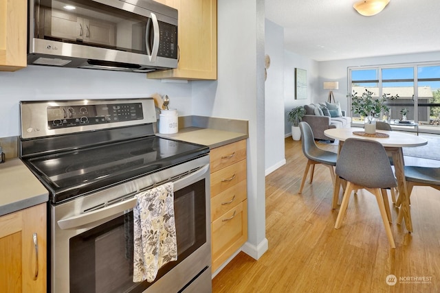 kitchen with appliances with stainless steel finishes, light brown cabinets, and light hardwood / wood-style floors