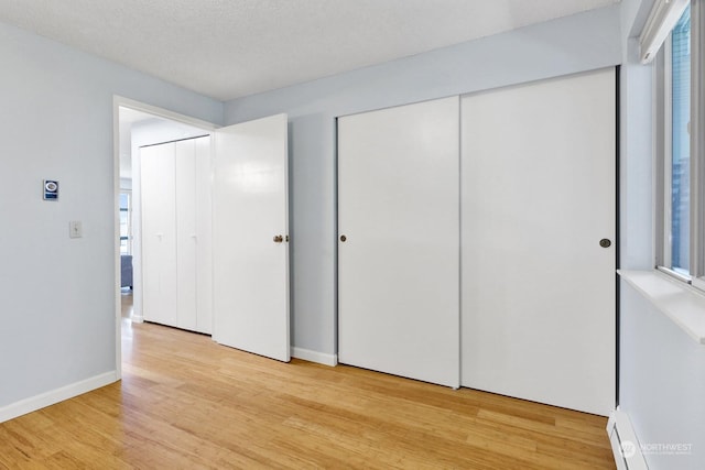 unfurnished bedroom with a baseboard radiator, a textured ceiling, and light wood-type flooring