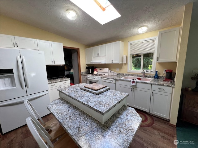 kitchen with sink, a textured ceiling, white appliances, vaulted ceiling with skylight, and white cabinets