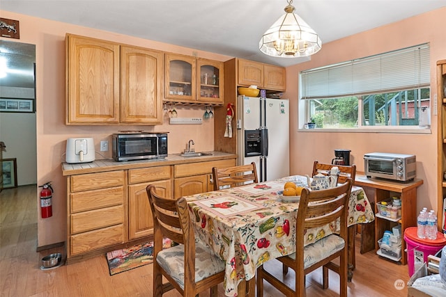 kitchen featuring pendant lighting, sink, light hardwood / wood-style flooring, white refrigerator with ice dispenser, and tile counters