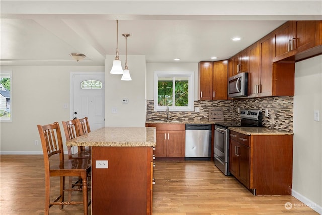 kitchen featuring a kitchen breakfast bar, hanging light fixtures, a center island, light stone counters, and stainless steel appliances