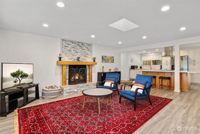 living room with a skylight, a stone fireplace, and light hardwood / wood-style flooring