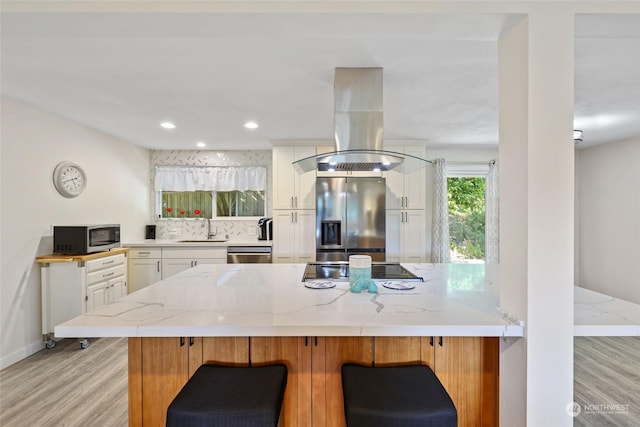 kitchen with stainless steel appliances, island exhaust hood, white cabinets, and kitchen peninsula