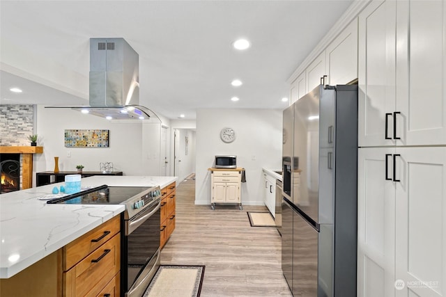 kitchen with white cabinetry, light stone counters, light hardwood / wood-style flooring, island exhaust hood, and stainless steel appliances