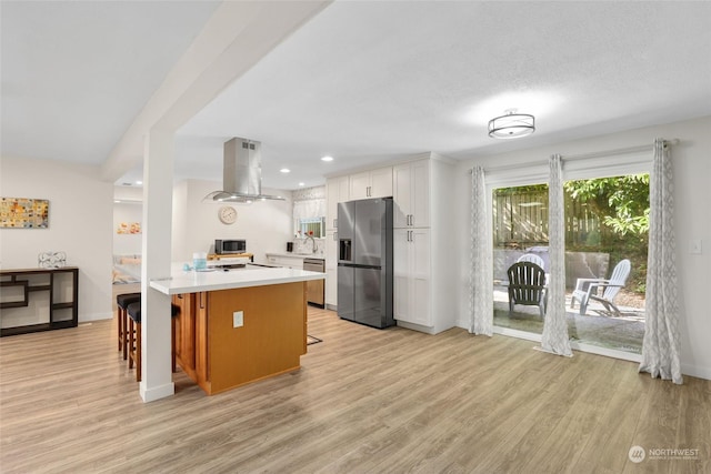 kitchen featuring appliances with stainless steel finishes, island range hood, white cabinets, a kitchen breakfast bar, and kitchen peninsula