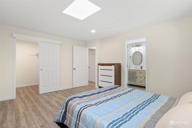 bedroom with a walk in closet, ensuite bath, a skylight, a closet, and hardwood / wood-style flooring