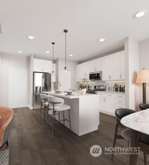 kitchen featuring white cabinets, appliances with stainless steel finishes, decorative light fixtures, dark hardwood / wood-style flooring, and a kitchen island with sink