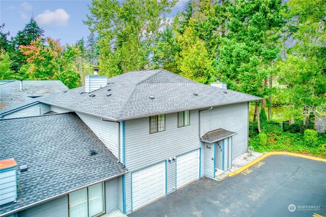 exterior space featuring a shingled roof, a chimney, an attached garage, and aphalt driveway