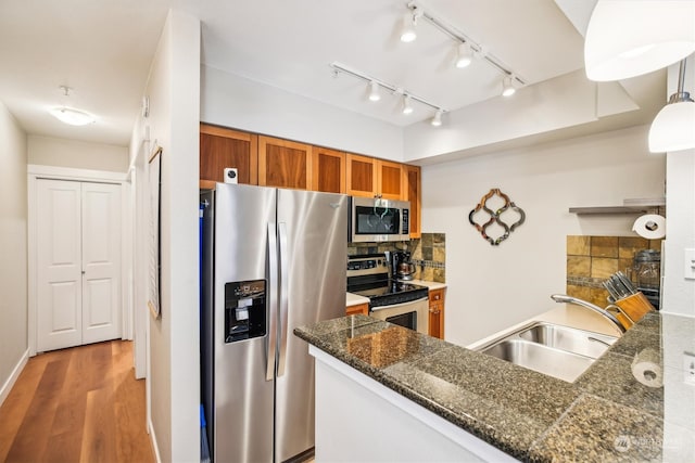 kitchen featuring rail lighting, hardwood / wood-style floors, appliances with stainless steel finishes, decorative light fixtures, and sink