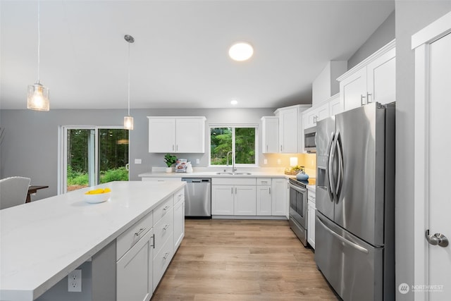 kitchen featuring light wood-style flooring, stainless steel appliances, a sink, white cabinets, and decorative light fixtures