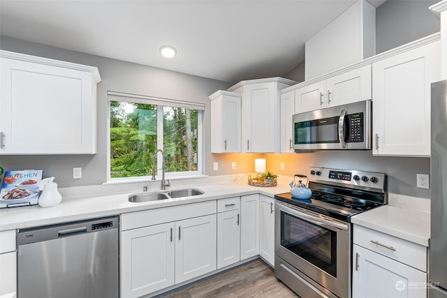 kitchen with white cabinets, stainless steel appliances, light countertops, light wood-style floors, and a sink