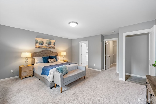 bedroom with light carpet, a spacious closet, baseboards, and ensuite bathroom