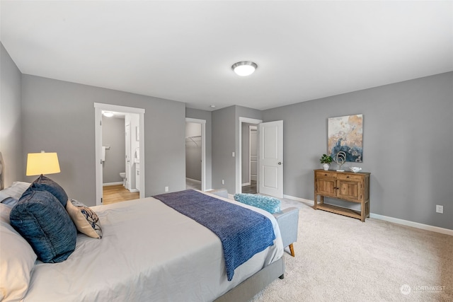 bedroom featuring light colored carpet, ensuite bath, a spacious closet, and baseboards