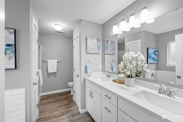 bathroom featuring visible vents, double vanity, a sink, and toilet